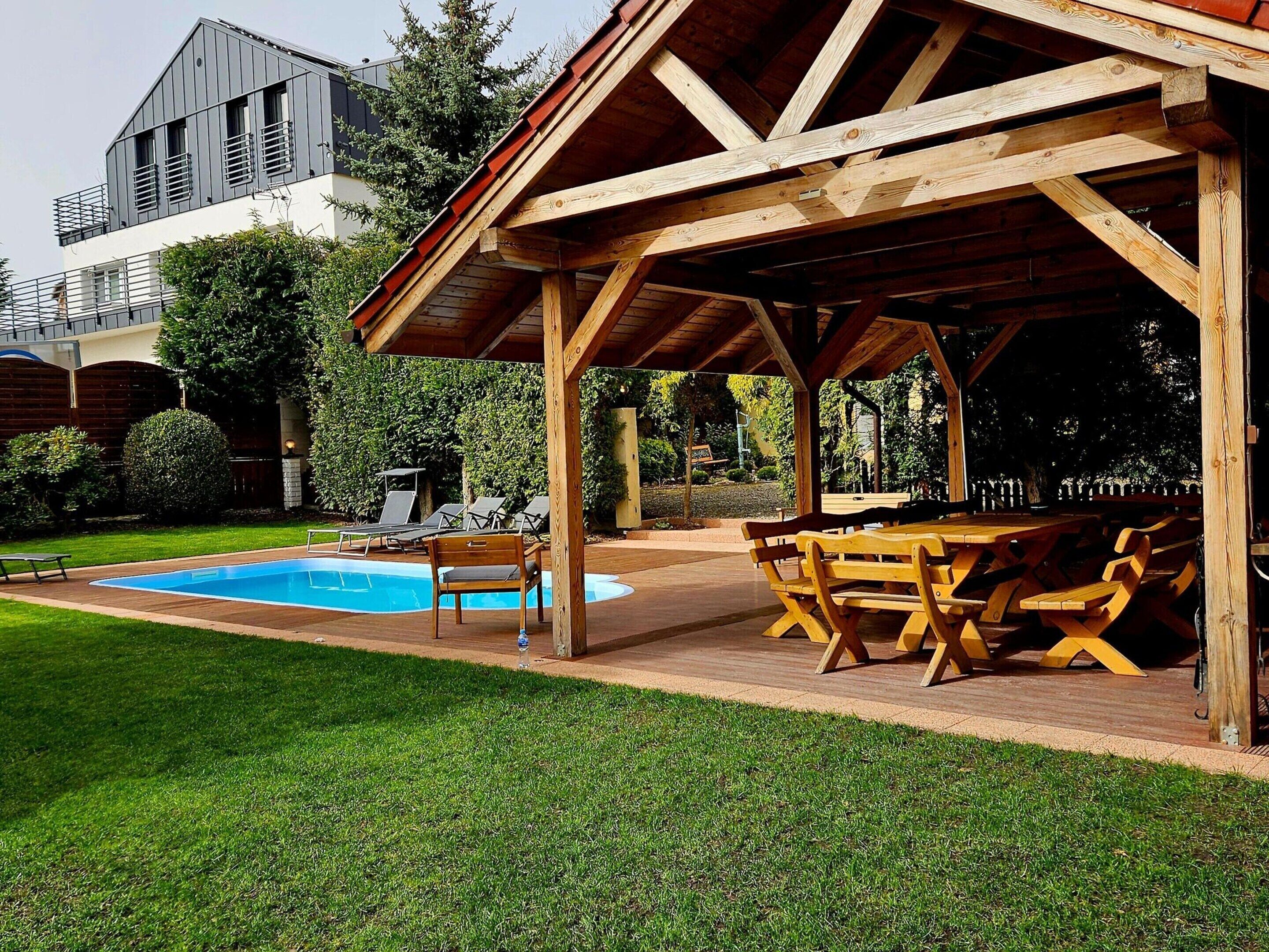 Un espacio al aire libre techado con piscina, sillas de descanso y una mesa de madera.