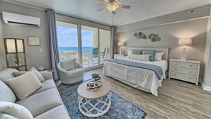 A modern bedroom with a large bed, a ceiling fan, a view of the ocean, and a round coffee table.