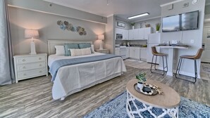 A modern bedroom with a bed, bedside tables, a desk, and a kitchenette.