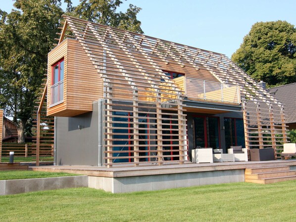 A modern house with a wooden exterior, a balcony, and a covered outdoor seating area. - Chalet in Wendorf (Kuhlen-Wendorf)