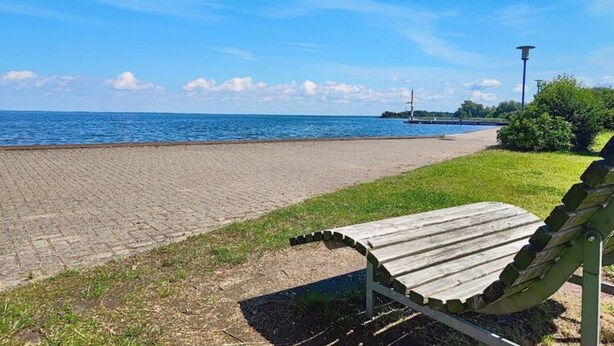 Ein gepflasterter Weg am Wasser mit einer Bank und einer Laterne.