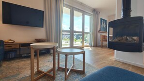 Ein modernes Wohnzimmer mit Kamin, Flachbildfernseher und einem großen Fenster mit Vorhängen.