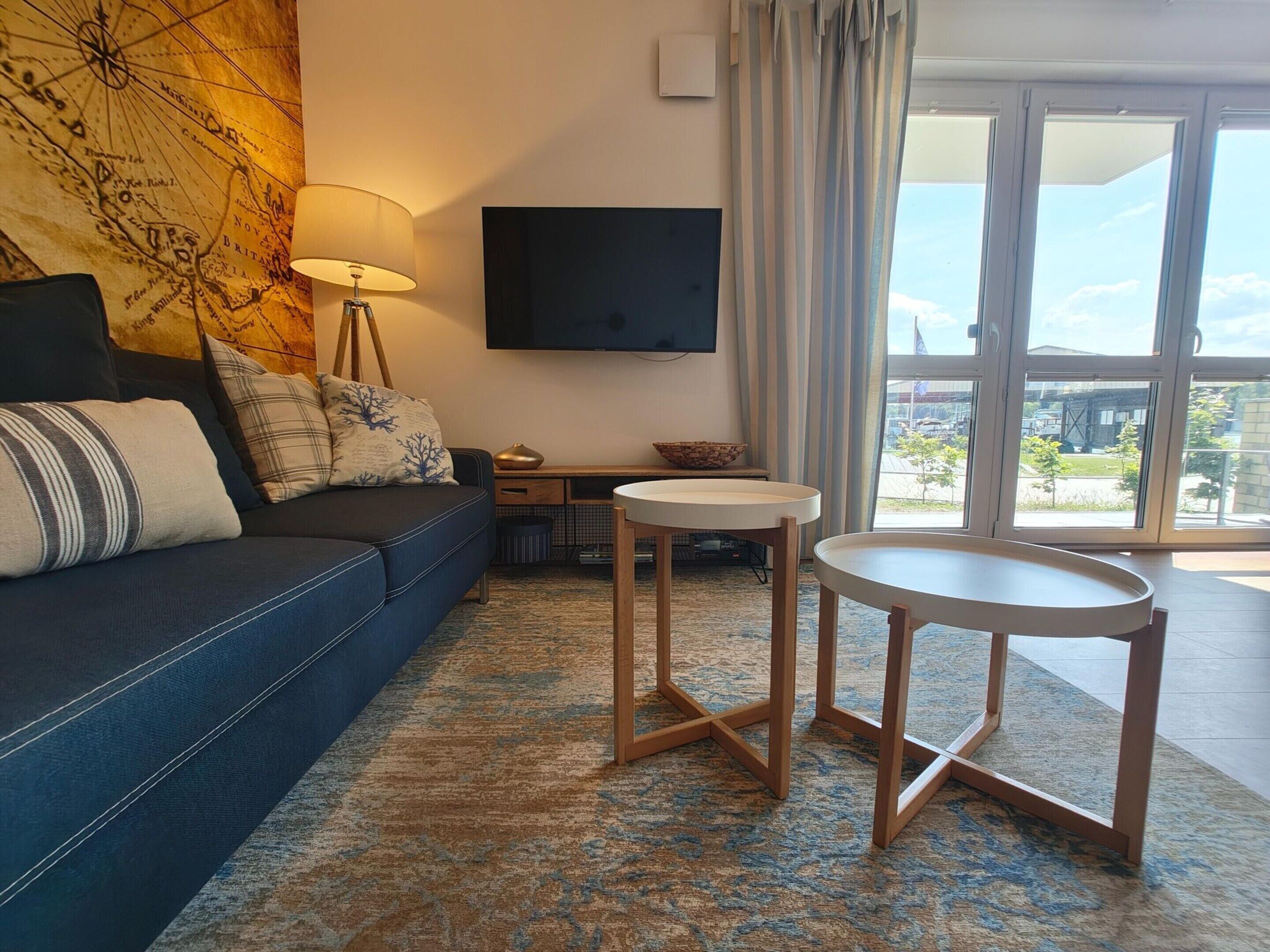 Un salon moderne avec un canapé, un téléviseur, une petite table et une vue dégagée grâce à de grandes fenêtres.