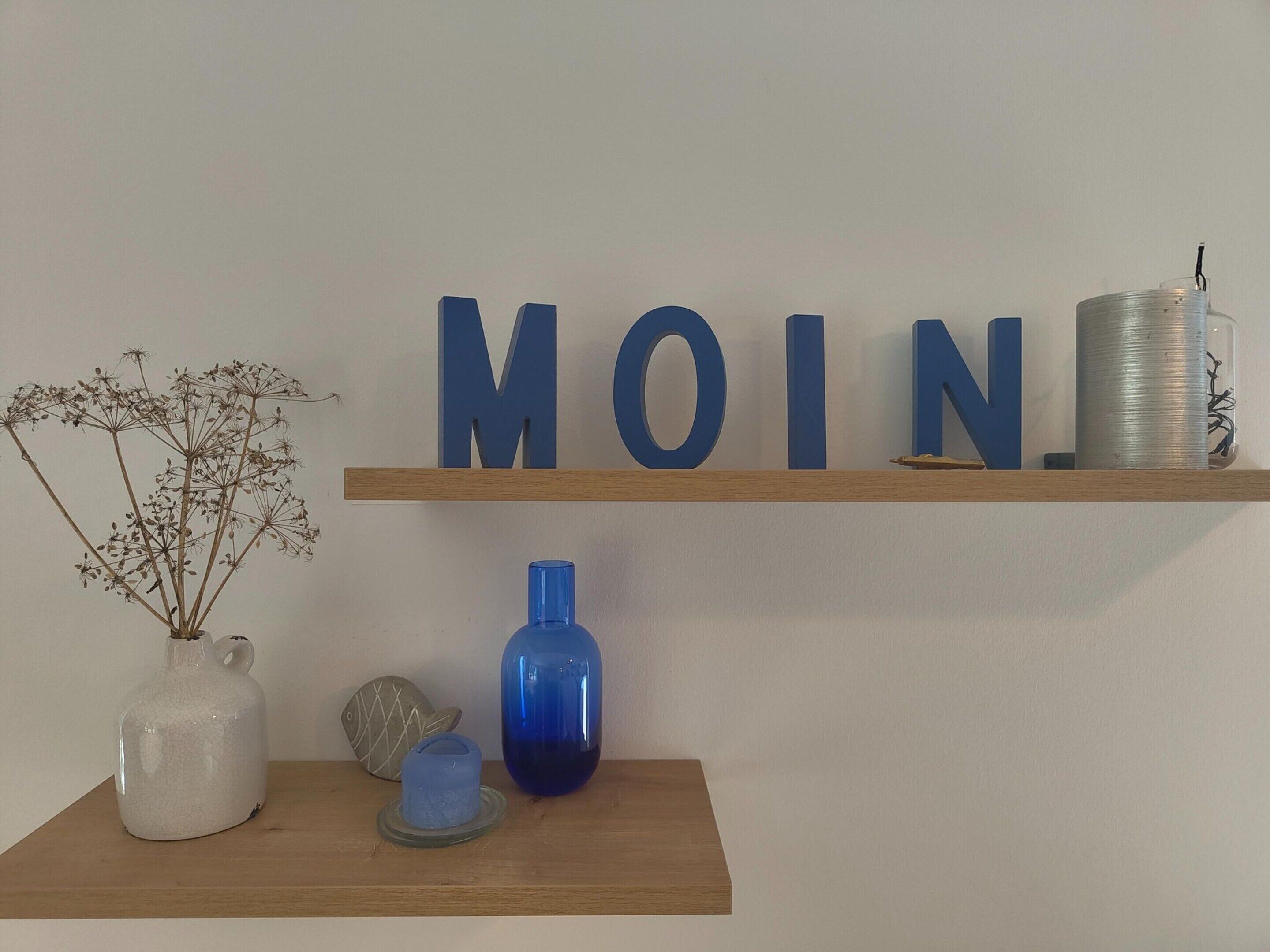 Une étagère en bois ornée d’objets décoratifs, notamment un pichet blanc, un vase bleu et un objet en forme de poisson.