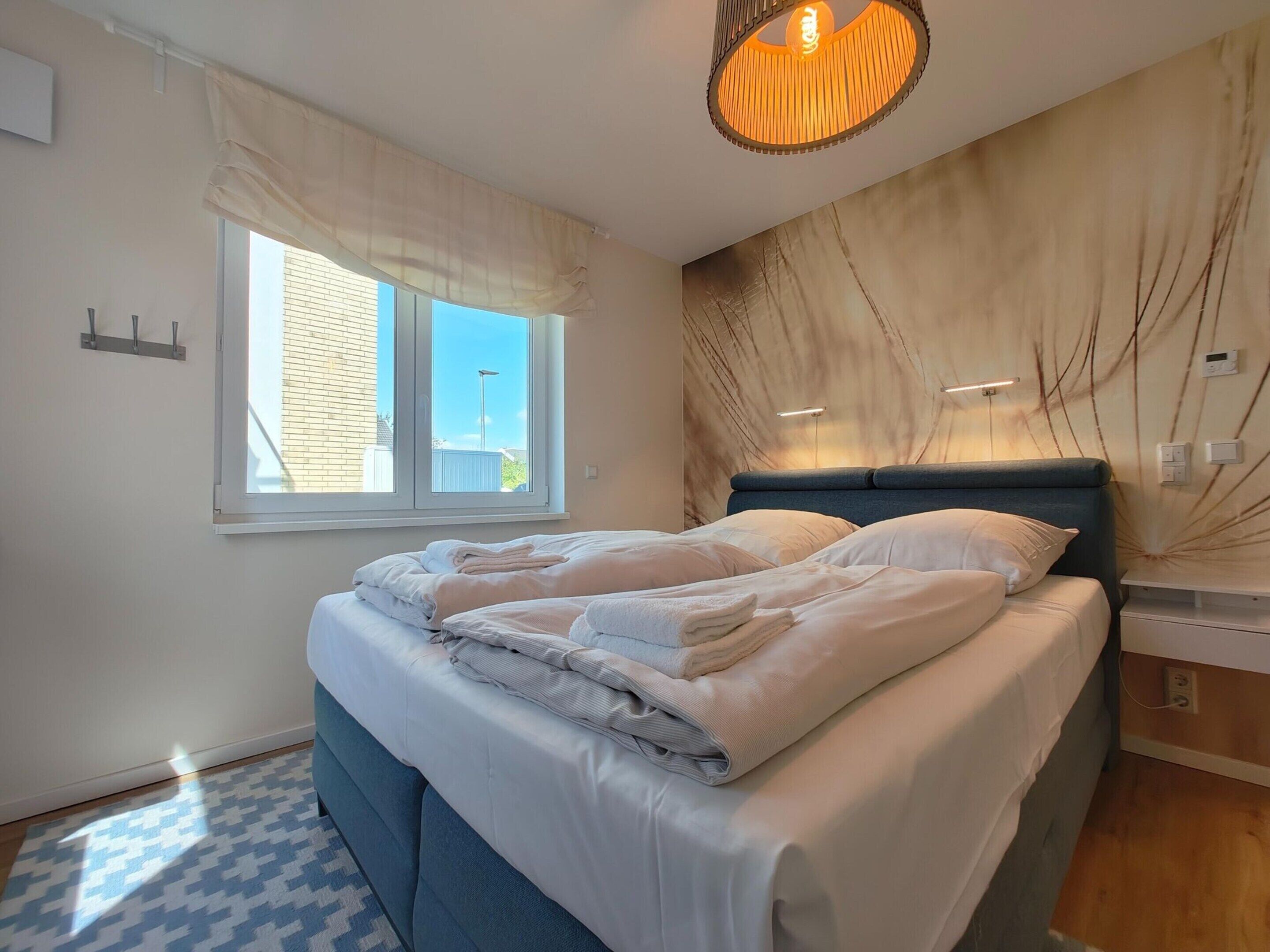 A modern bedroom with a large bed, a window with curtains, a marble-patterned wall, and a hanging light fixture.