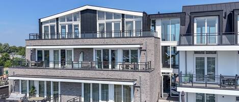 A modern multi-story residential building with balconies, large windows, and a flat roof.