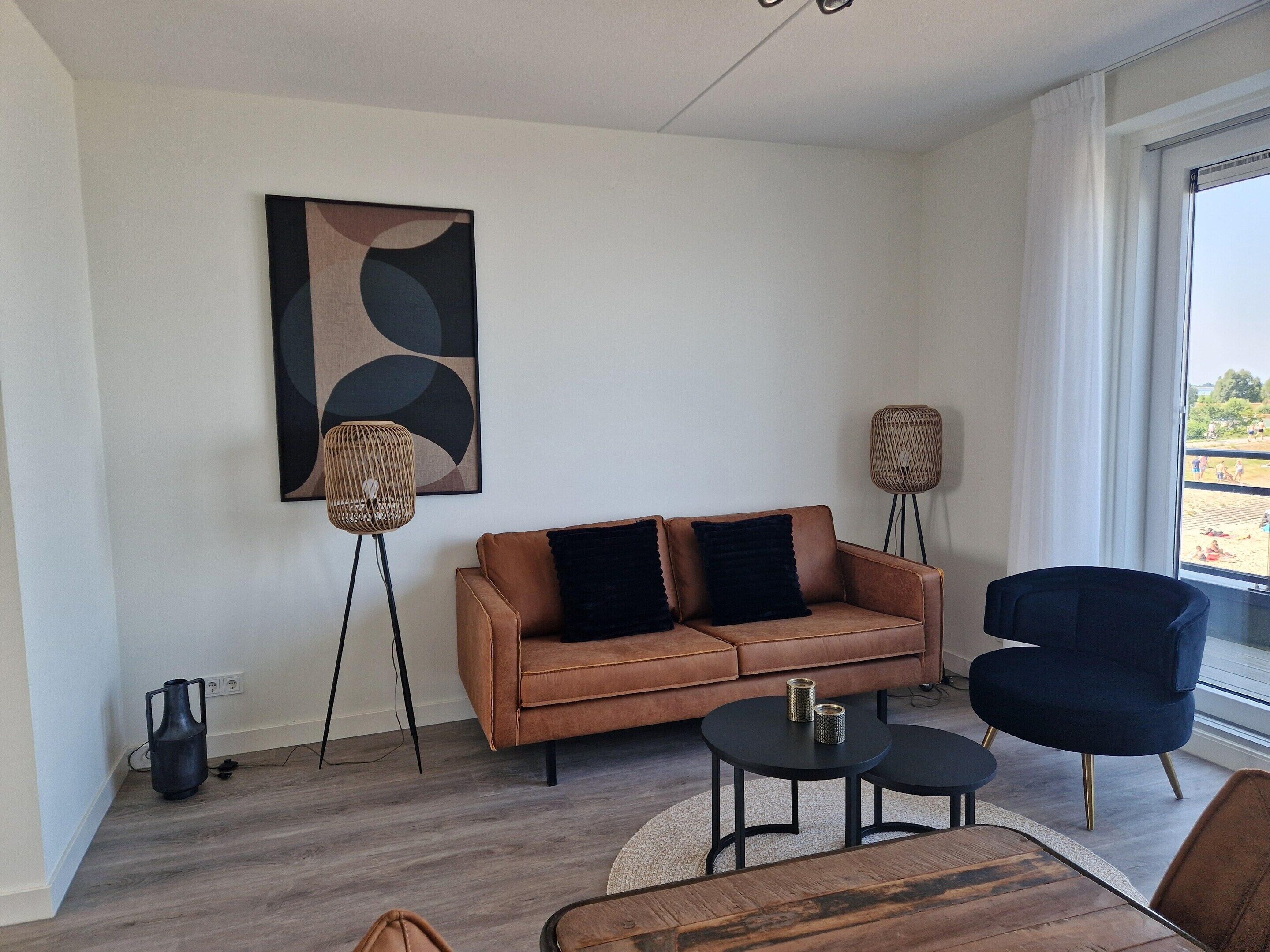 Uma sala de estar moderna com um sofá marrom, duas poltronas pretas, uma mesa de centro e um abajur.