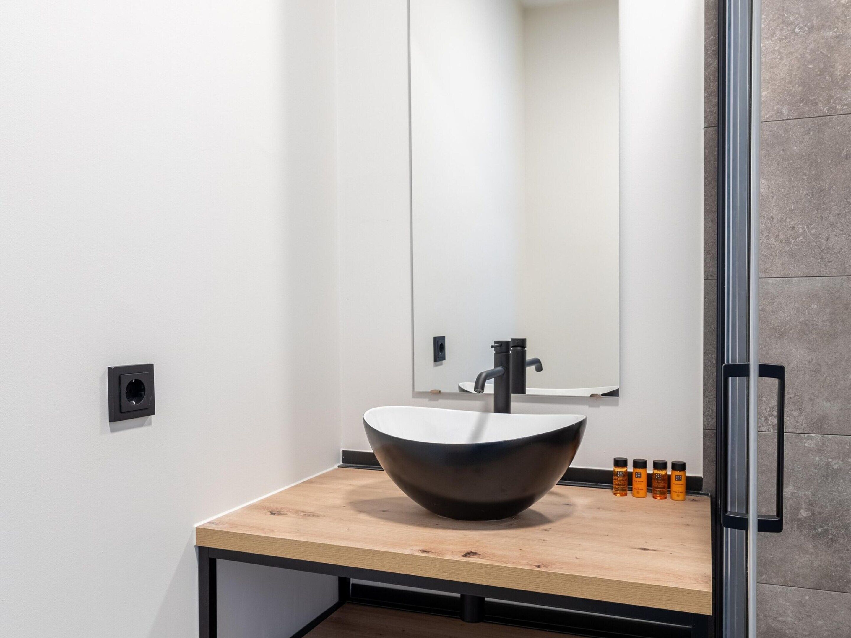 Un bagno moderno con un lavabo a incasso, uno specchio e un piano in legno.
