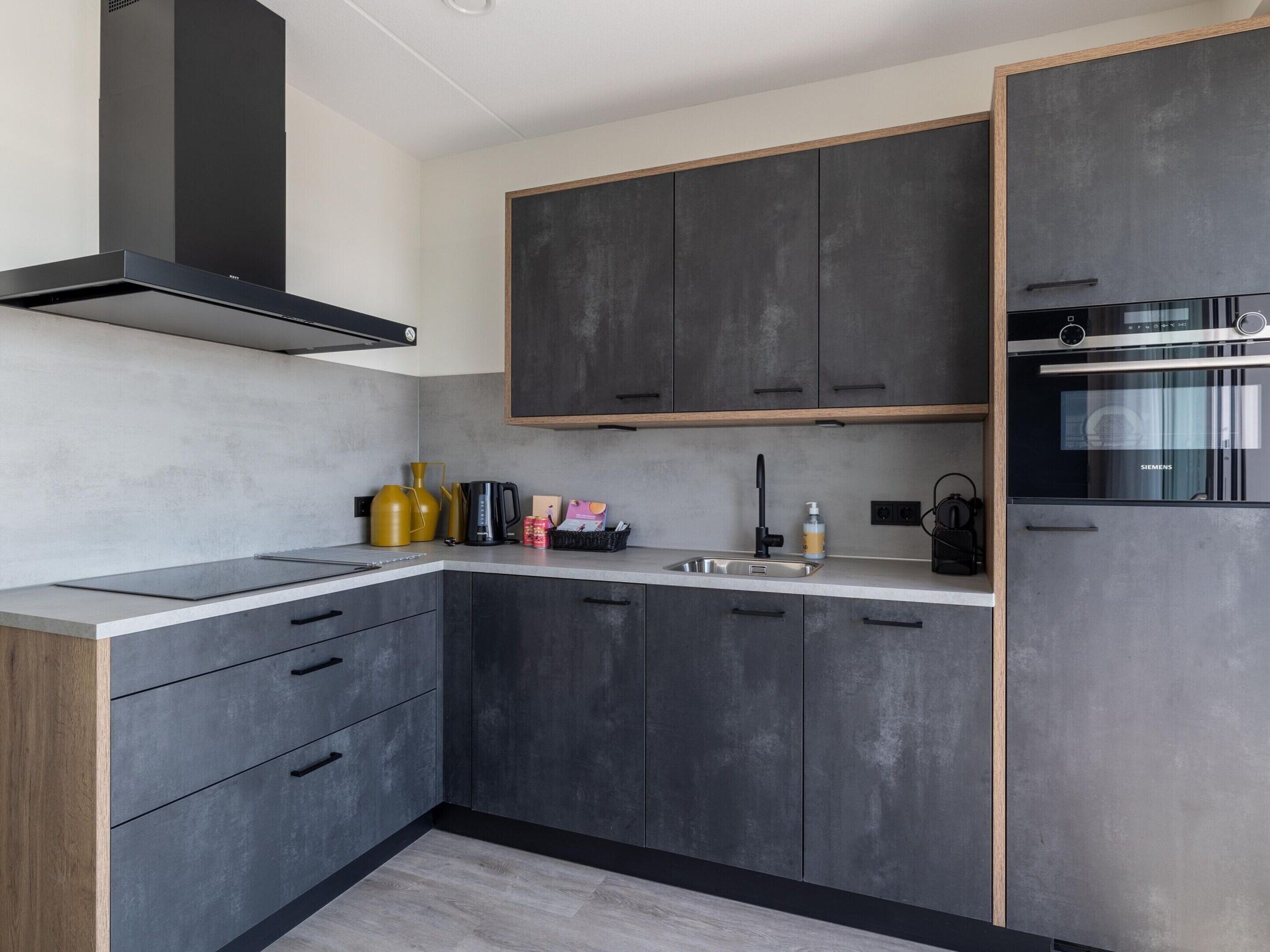 A modern kitchen with dark cabinets, a built-in oven, and a stainless steel range hood.