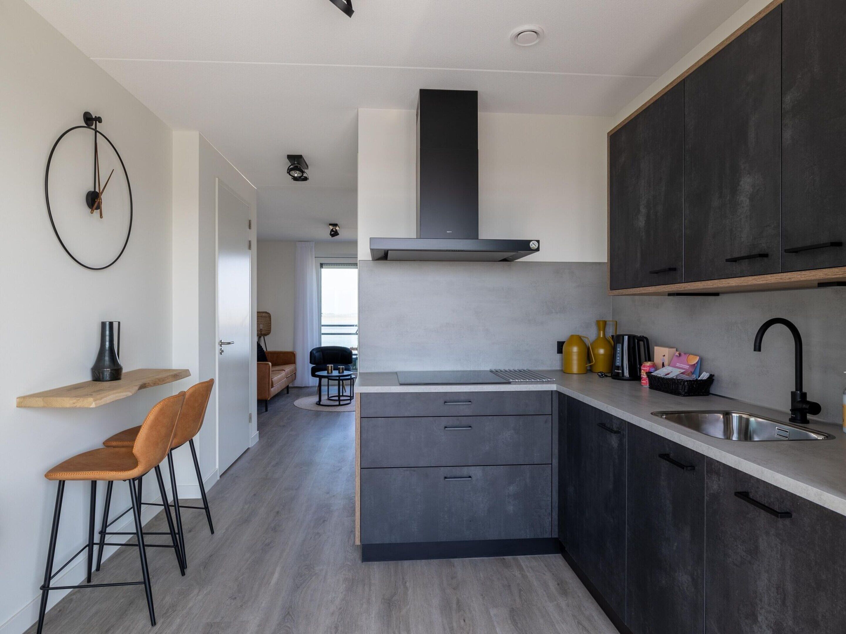 A modern kitchen with dark cabinets, a central island, and a dining area with a sofa and chairs.