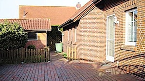Une maison en briques avec un toit en tuiles, une clôture en bois et une allée pavée.