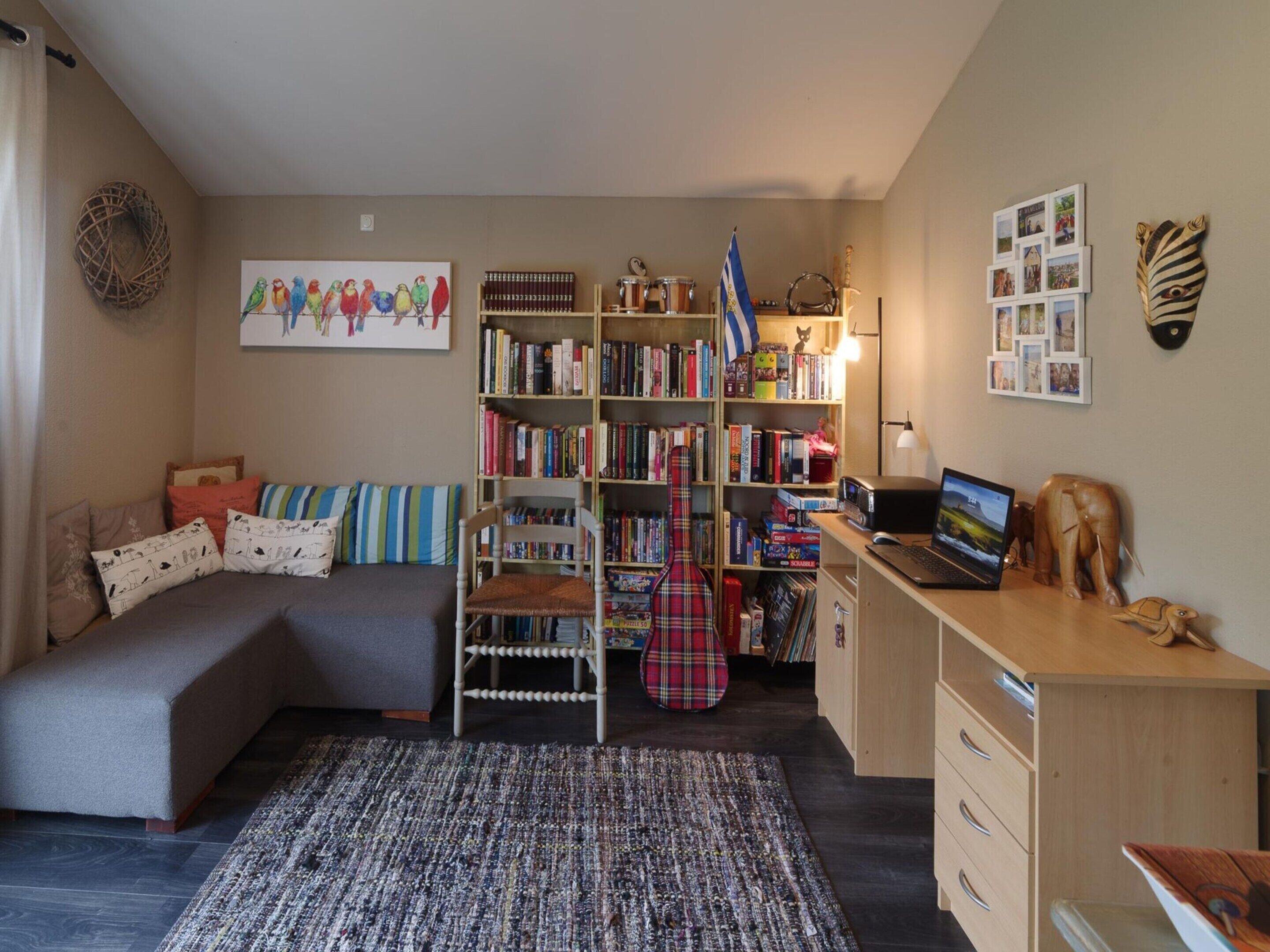 A cozy room with a sofa, a bookshelf, a desk with a laptop, and a guitar.