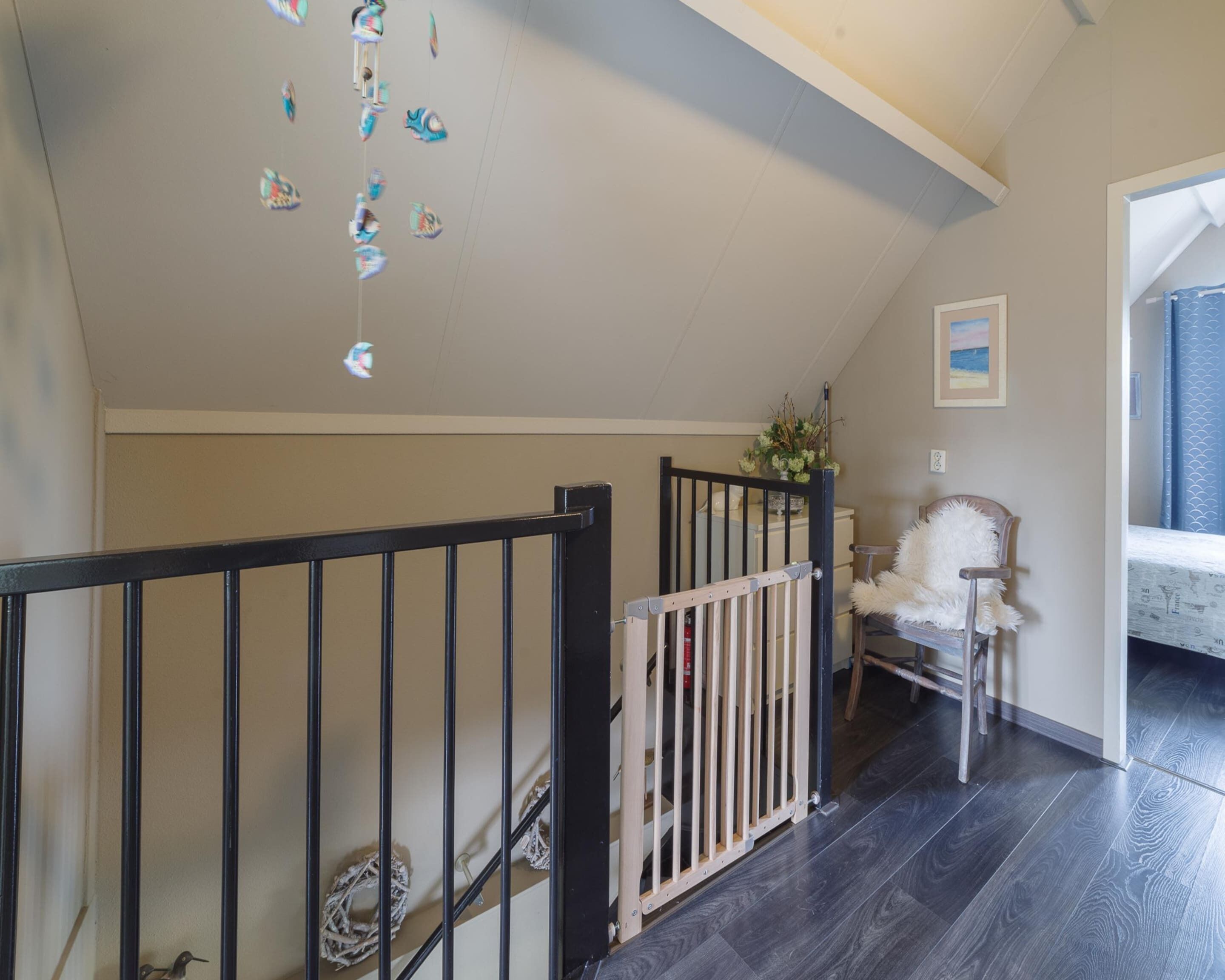 A staircase with a black railing, a white chair with a fluffy cushion, and a small bird on the floor.