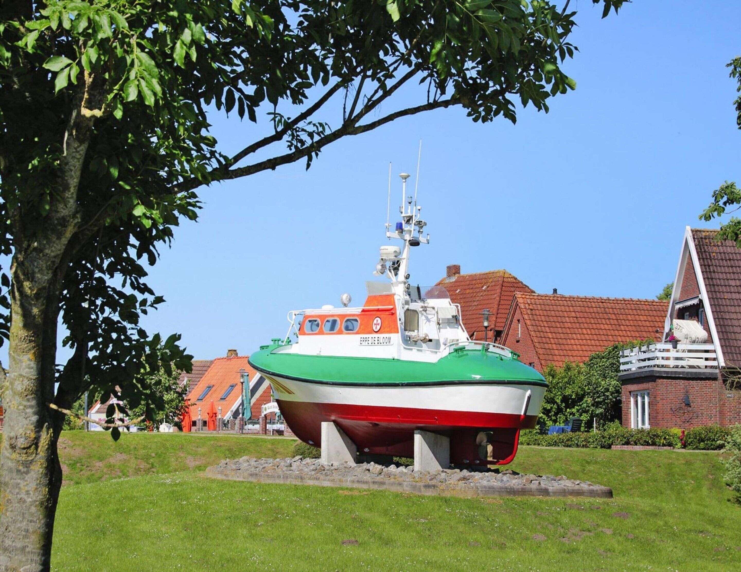A green and white boat on display, surrounded by a grassy area and buildings in the background.