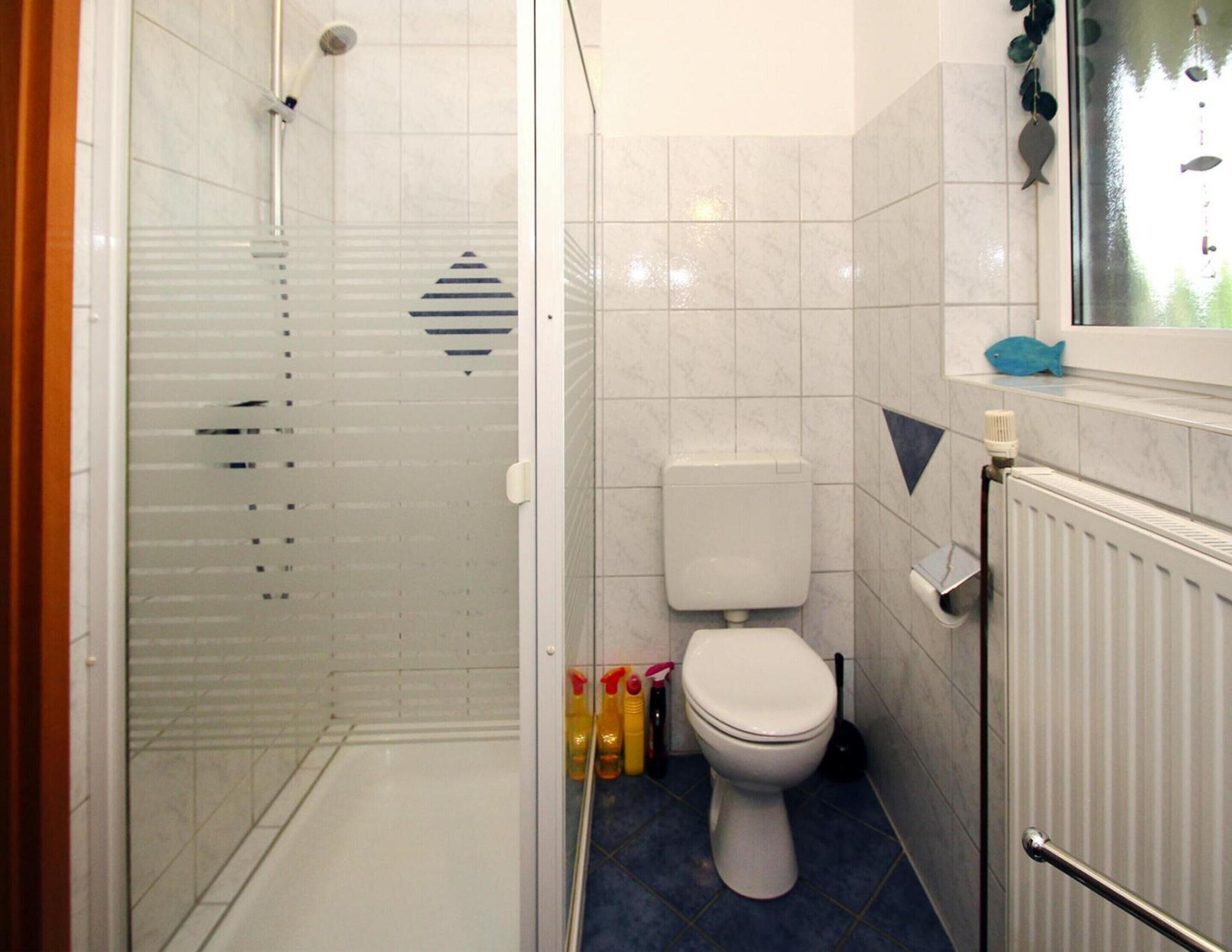 A bathroom with a glass shower enclosure, a toilet, and a radiator.