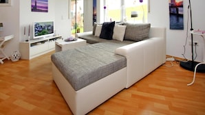 Un moderno salón con un sofá blanco, un televisor y un ventanal con vistas al exterior.