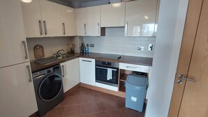 A compact kitchen with a washing machine, oven, and a small trash bin.