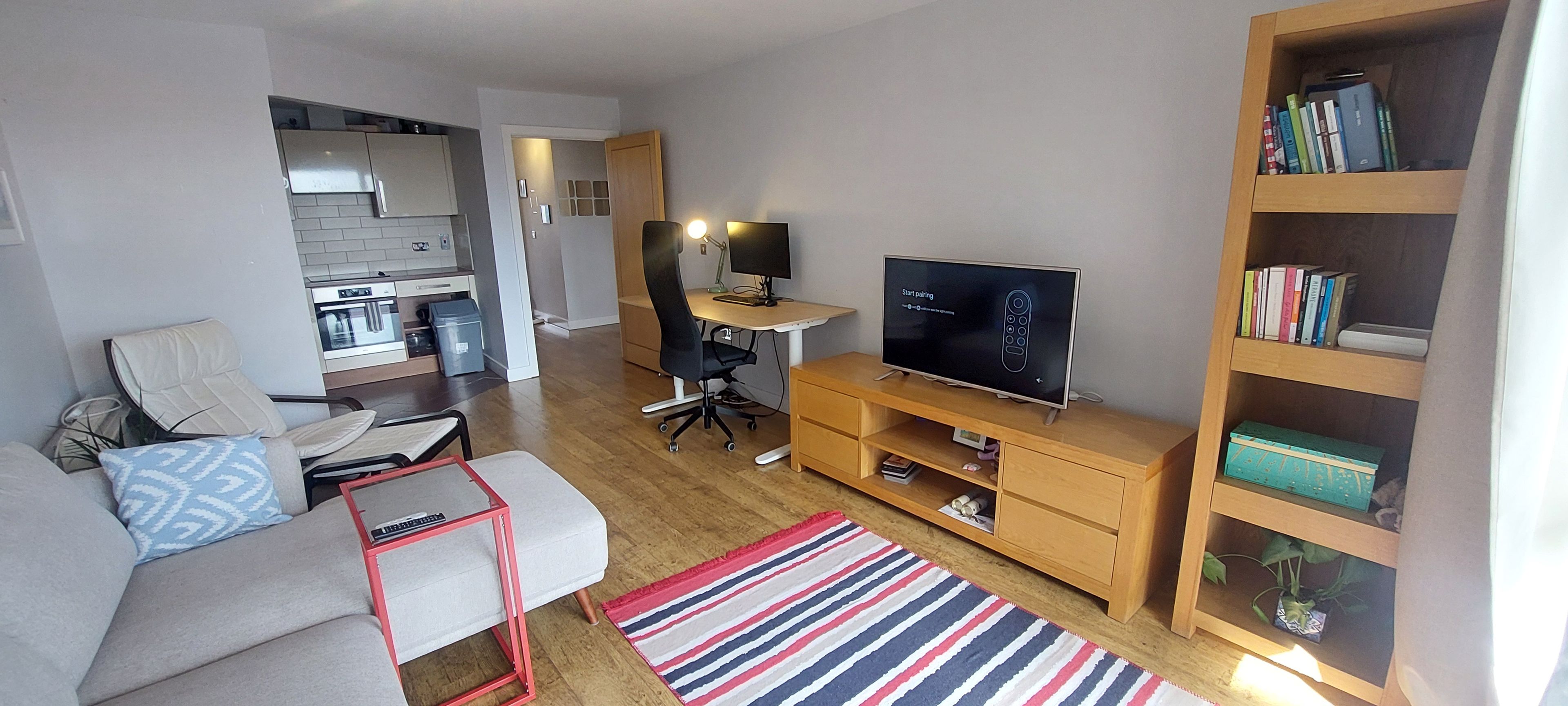 A modern living room with a sofa, a coffee table, a TV, a bookshelf, and a kitchen in the background.