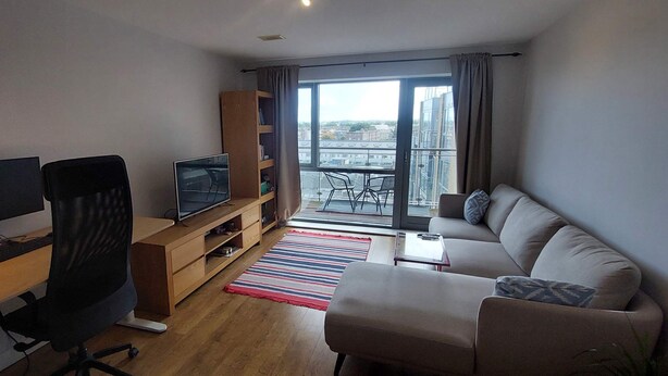 A modern living room with a flat-screen TV, a sofa, a coffee table, and a view of the city through large windows.