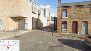 A narrow urban street with a mix of modern and traditional buildings, a gated entrance, and a clear road.