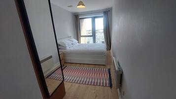 A bedroom with a bed, a window with curtains, a radiator, and a striped rug.