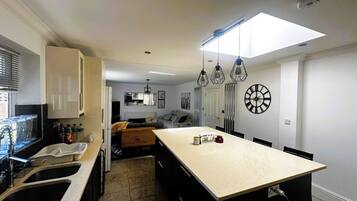 A modern kitchen with a central island, a dining area with a large clock, and a living space with a sofa and a coffee table.