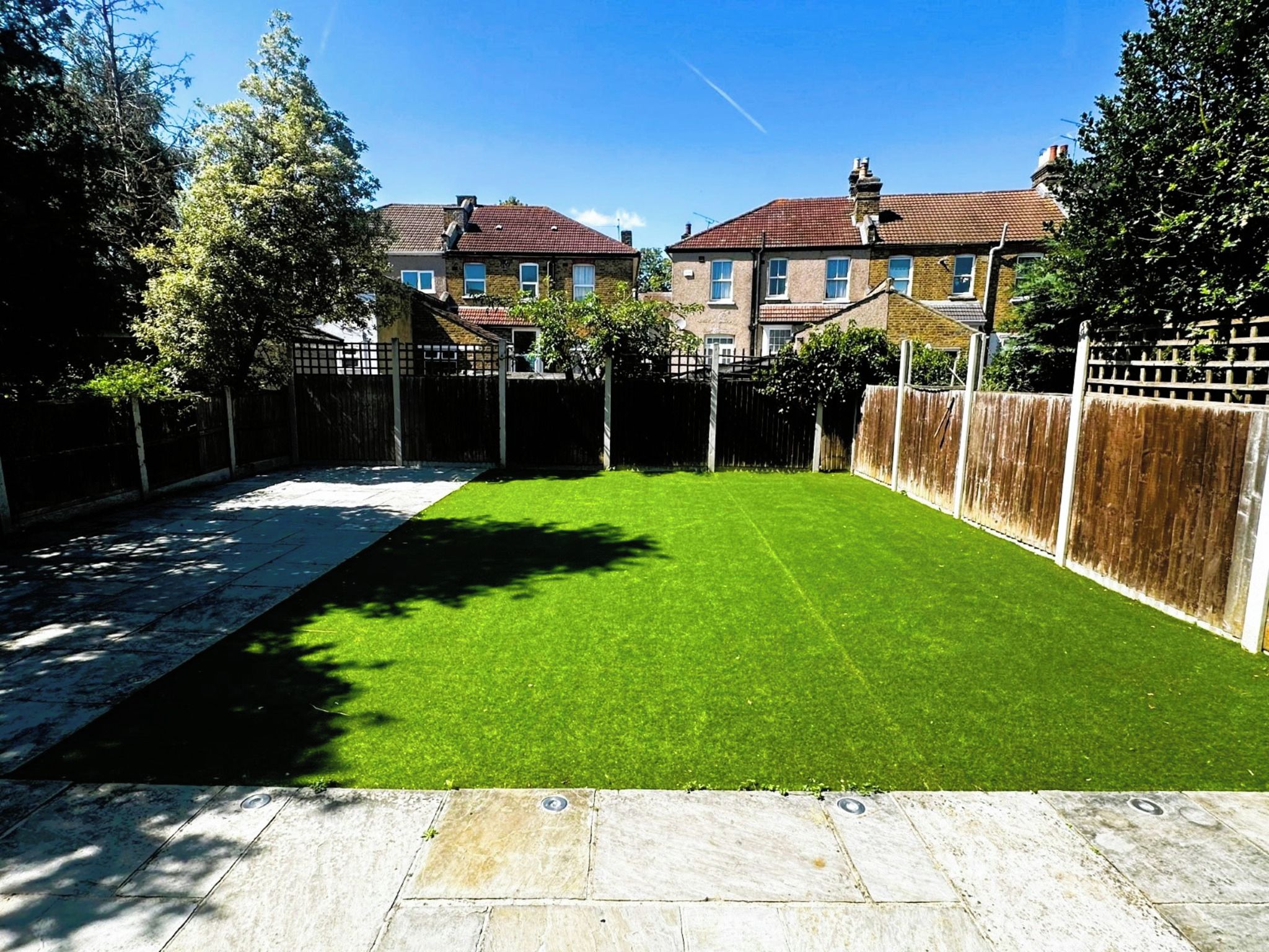 A backyard with a well-maintained lawn, a paved patio, and a wooden fence.