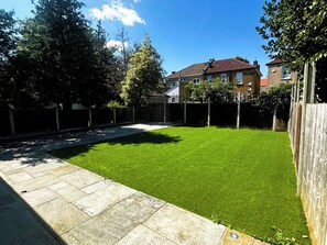 Un patio trasero con un césped cuidado, un sendero de piedra y una valla de madera.