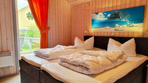 A bedroom with a bed, wooden walls, a painting, and a window with curtains.