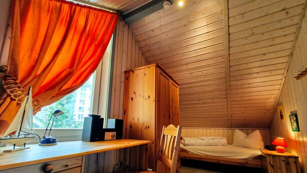 Una habitación acogedora tipo cabaña con un escritorio de madera, una silla, una cama y un armario.