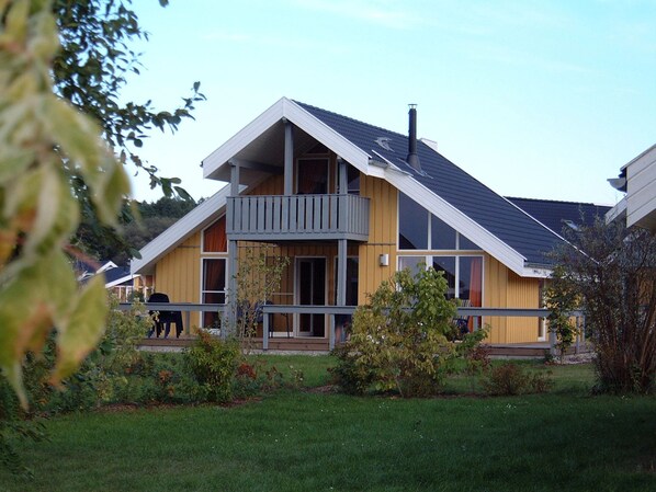 Une maison moderne à deux étages, dotée d’un balcon, d’une cheminée et d’une pelouse bien entretenue.