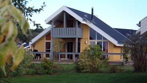 A modern two-story house with a balcony, a chimney, and a well-maintained lawn.