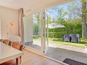 A modern room with a sliding glass door leading to a patio. The room has a dining table with chairs, a sofa, and a large window with curtains. - Holiday Home in Biggekerke Near Seabeach (Biggekerke)