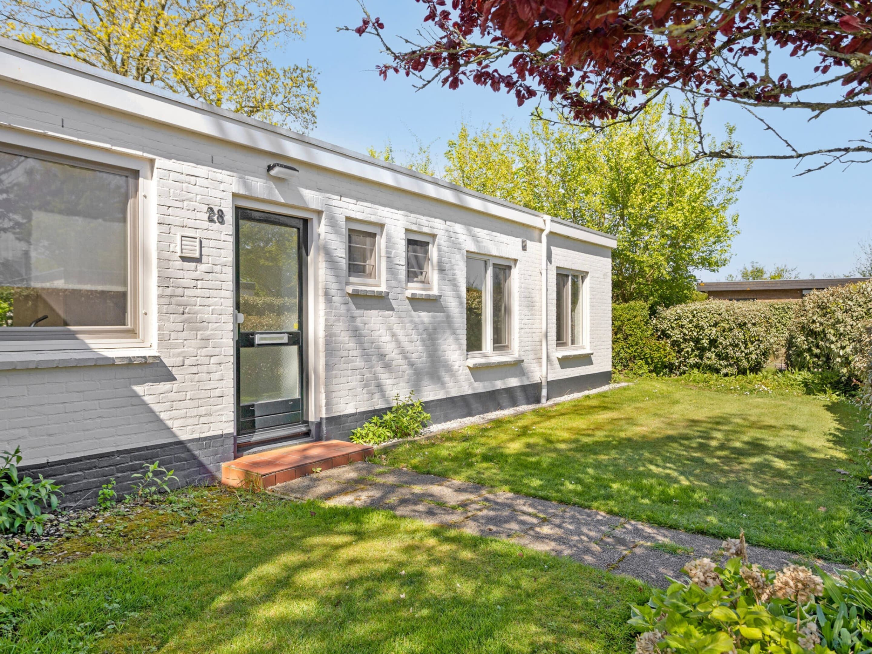 A modern single-story house with a white exterior, a front door, and a small front yard with a pathway leading to the door.