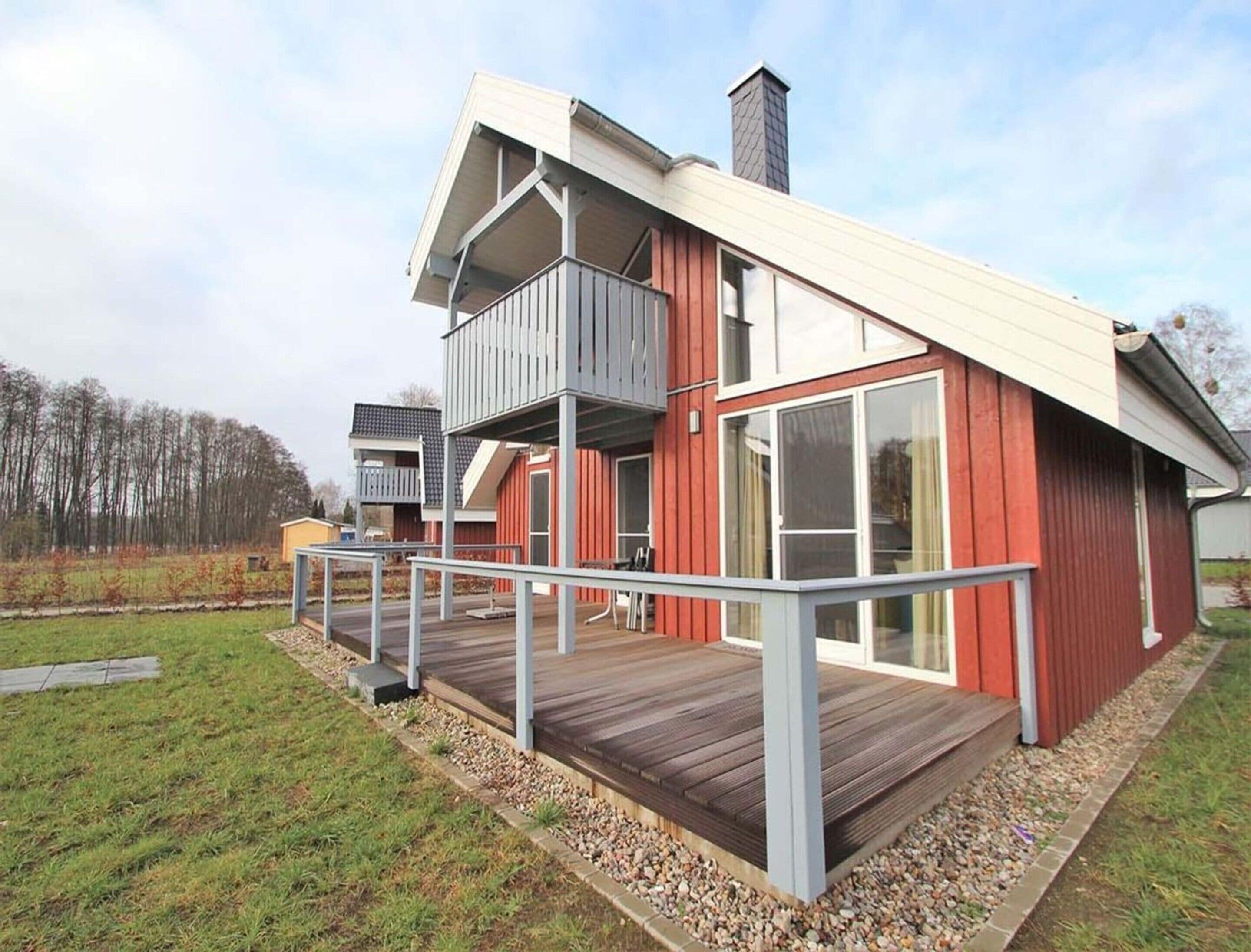 A modern two-story house with a wooden deck, large windows, and a red exterior.