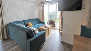 A modern living room with a blue sofa, a small table, and a TV mounted on the wall. - Ferienhaus im Ferienpark Mirow (Mirow)