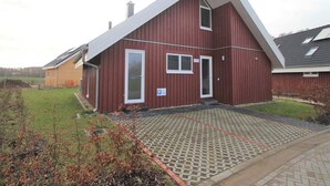 A red two-story house with a sloped roof, a front door, and a small porch. - Ferienhaus im Ferienpark Mirow (Mirow)