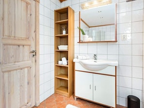 A bathroom with a wooden door, a white sink, a mirror, and a shelf with towels. - 5 Star Holiday Home in Treungen (Nissedal)