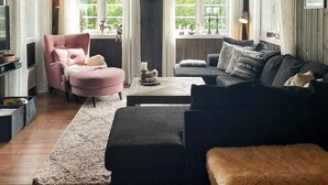 A cozy living room with a pink armchair, a dark sofa, and a coffee table. There are windows with curtains, a fireplace, and a TV on a stand. - 5 Star Holiday Home in Treungen (Nissedal)