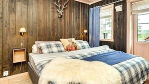 A bedroom with a wooden wall, a mounted deer head, a bed with plaid bedding, a fur throw, and two bedside lamps. - 5 Star Holiday Home in Treungen (Nissedal)