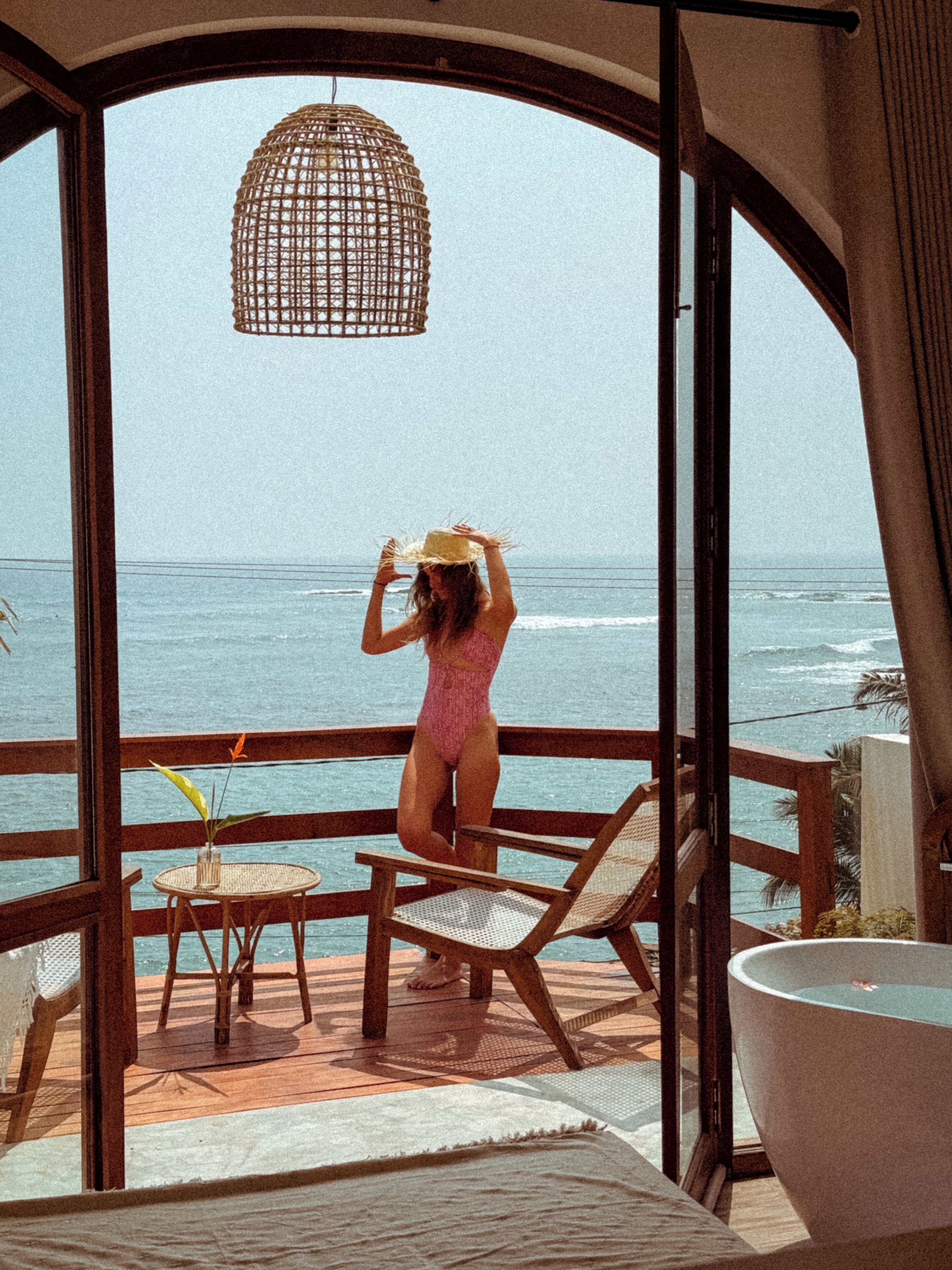 A woman in a swimsuit on a balcony overlooking the ocean.