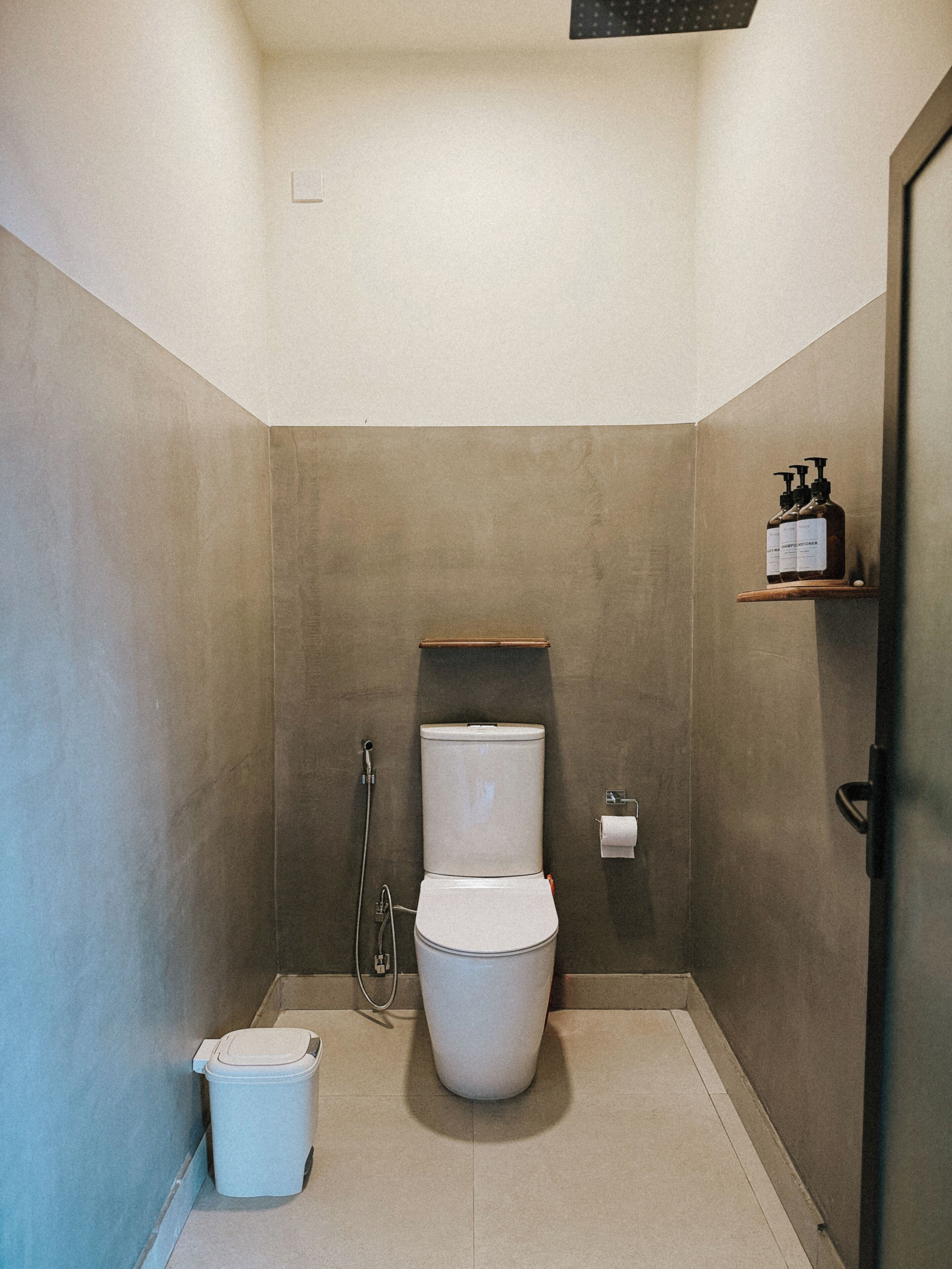 Un baño pequeño y moderno con inodoro, ducha y un estante con artículos de tocador.