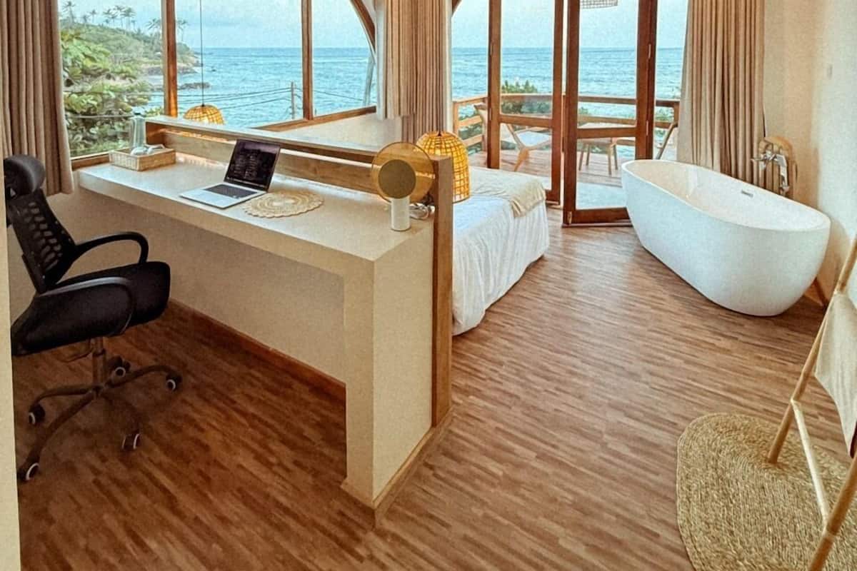 Une chambre moderne avec une grande fenêtre, un bureau, un ordinateur portable, un lit, une baignoire et un ventilateur de plafond.