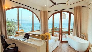 A modern bedroom with a large window, a desk, a laptop, a bed, a bathtub, and a ceiling fan.