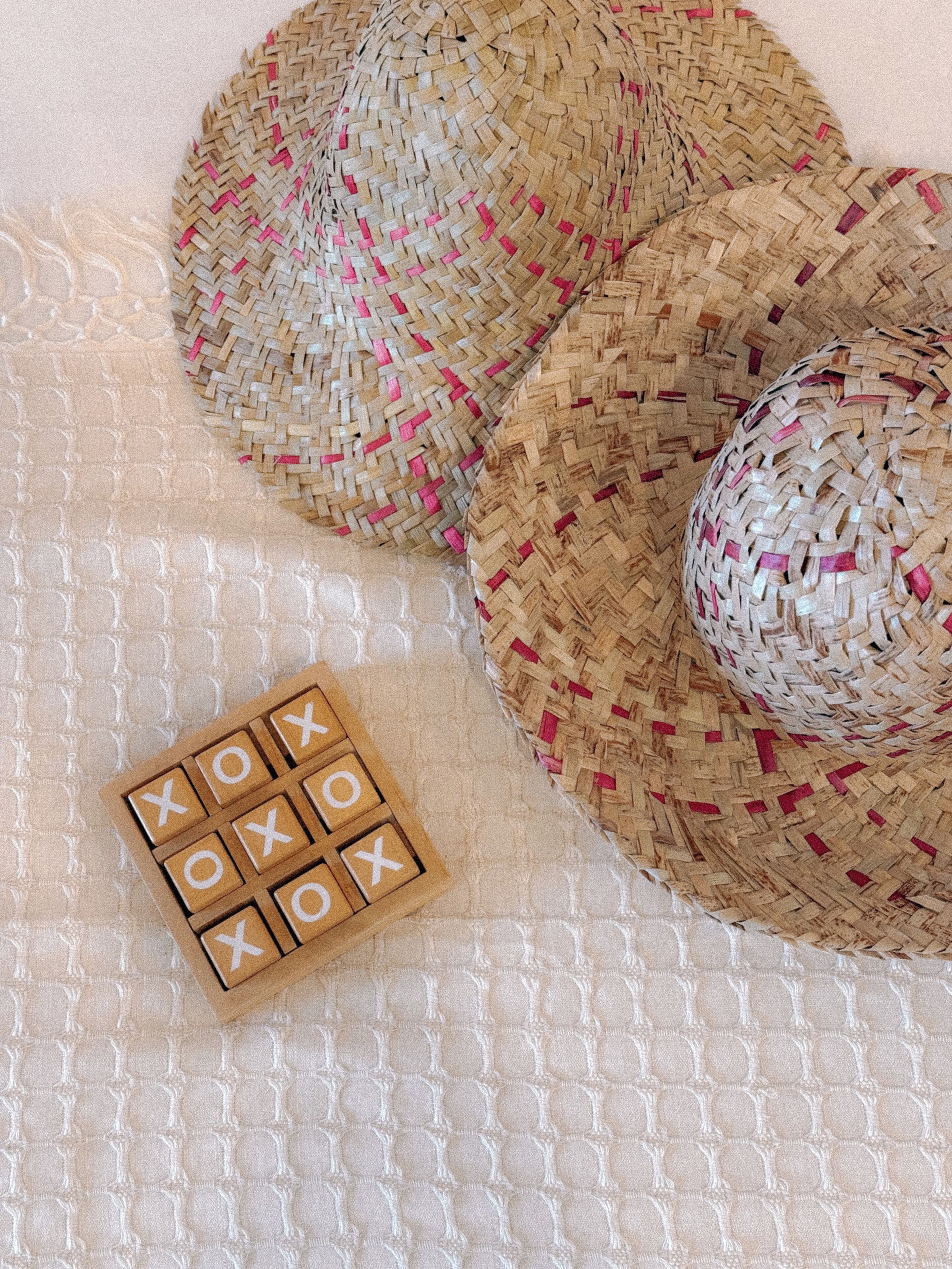 Woven hats and a tic-tac-toe game on a textured fabric.