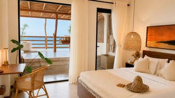 A bedroom with a bed, a desk, a chair, a large window with a view of the sea, and a hanging light fixture.