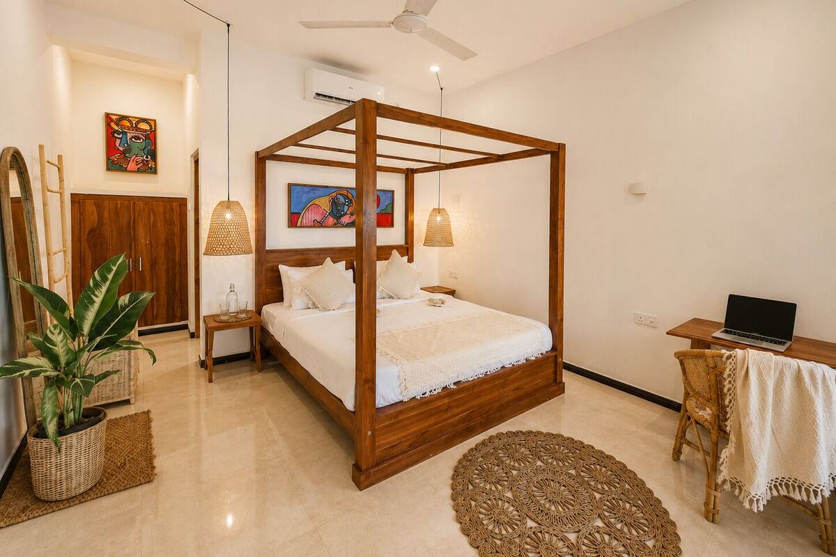 Une chambre à coucher avec un lit à baldaquin, un bureau avec un ordinateur portable, une plante en pot et un tapis tissé.