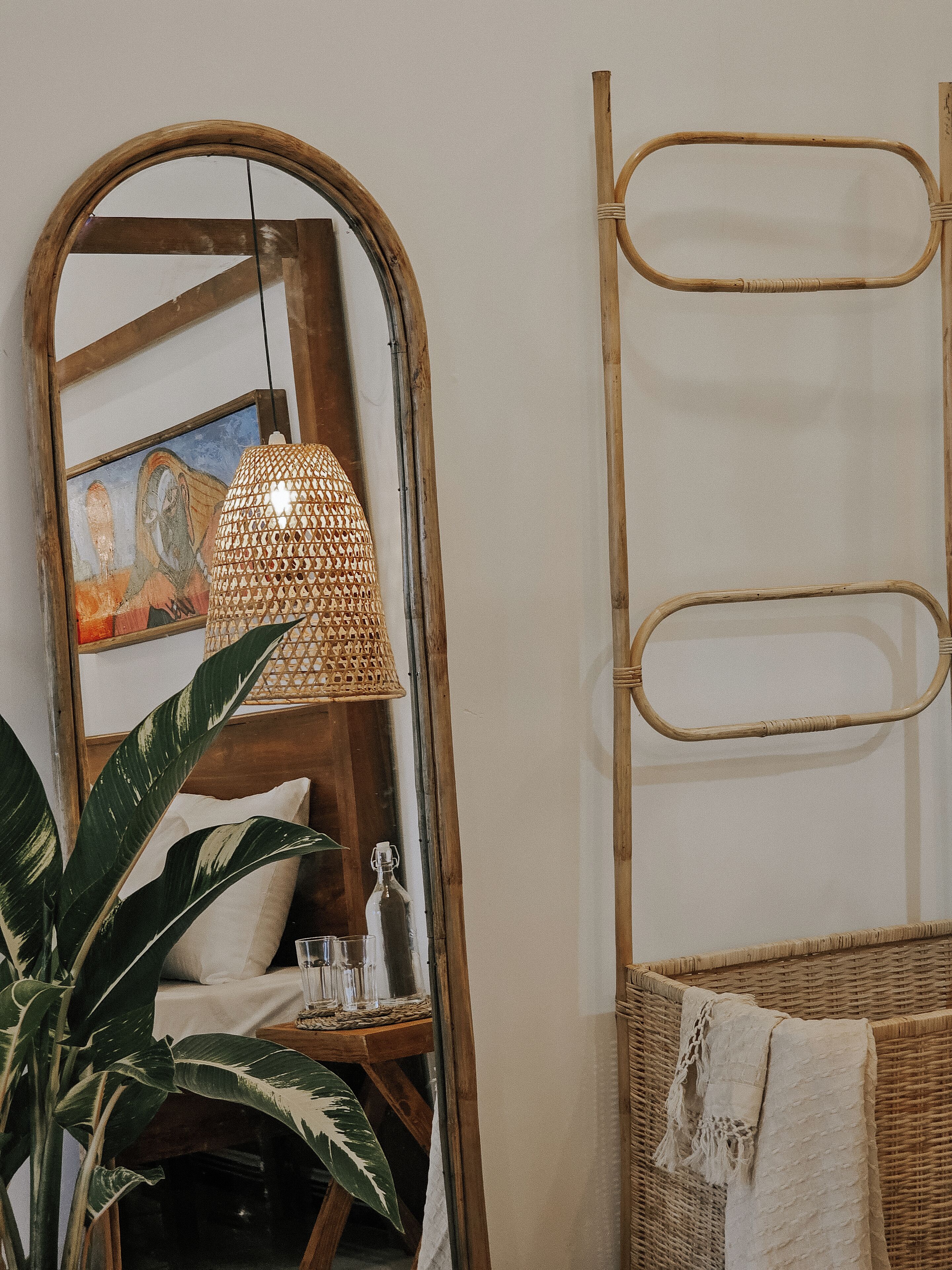 Una habitación con un espejo grande, una silla de mimbre, una lámpara colgante y una planta.