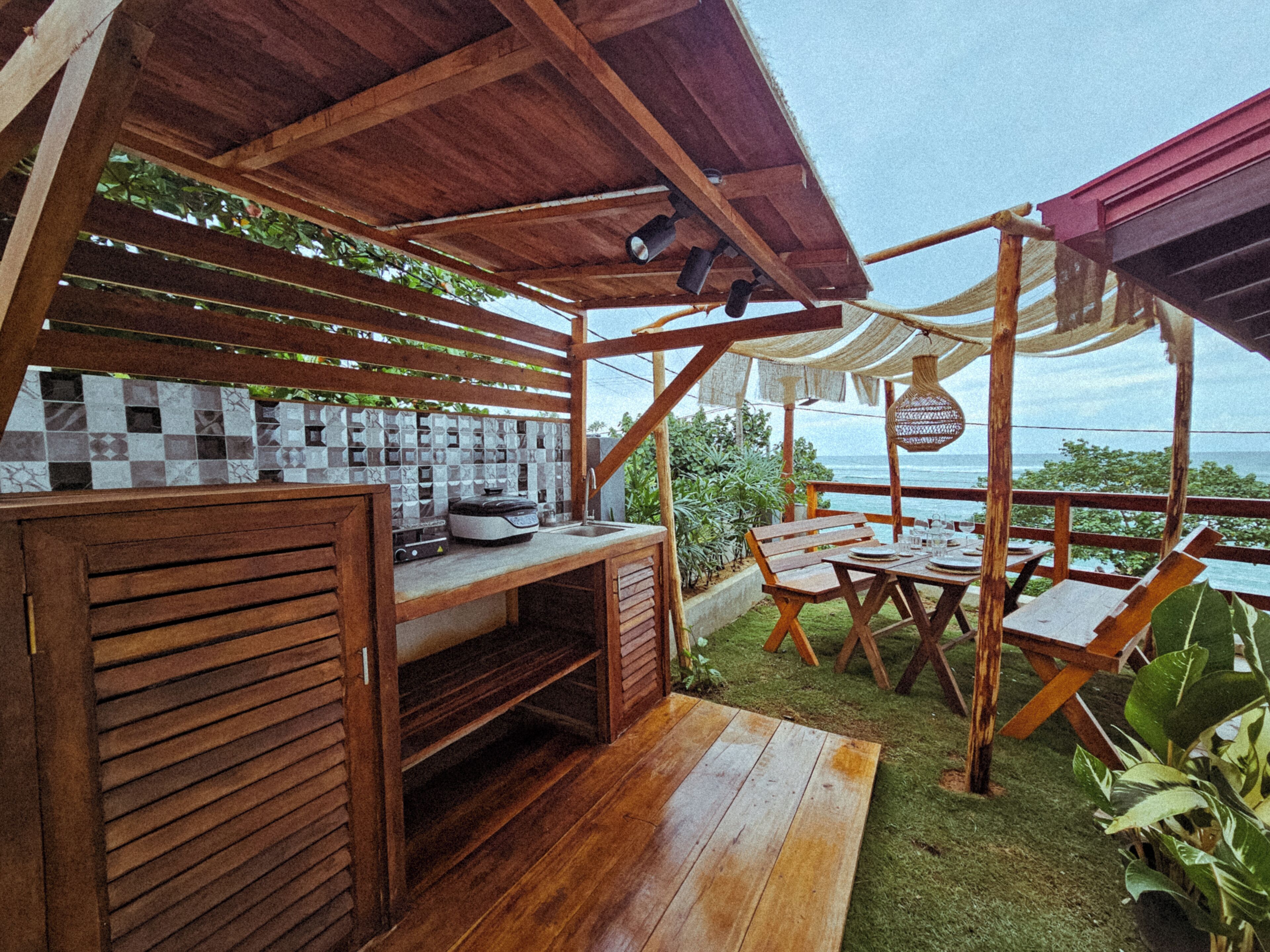 Eine Holzdachterrasse mit Küchenzeile, Sitzgelegenheit und Meerblick.