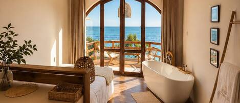 A modern bathroom with a freestanding bathtub, a vanity with a mirror, and a view of the ocean.